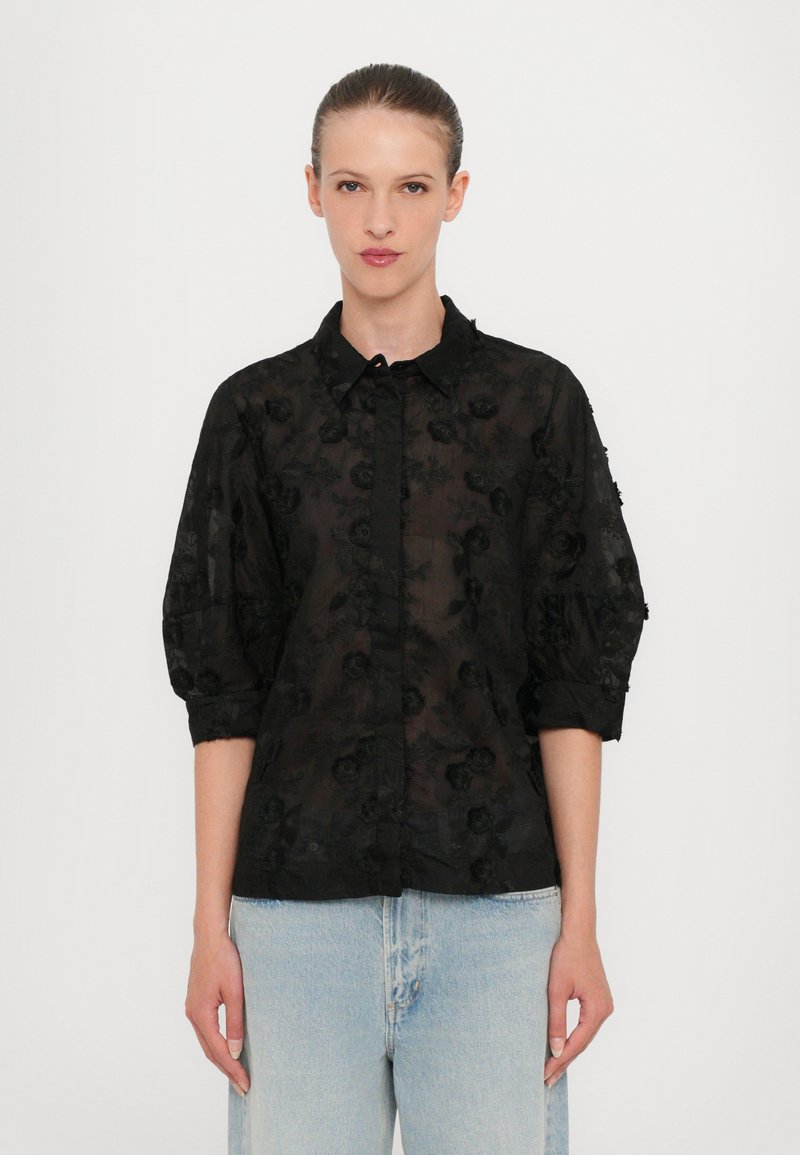 Sort gennemsigtig skjorte med blomsterbroderi, knap-front, opfoldede ærmer og klassisk krave. Casual pasform sat sammen med lyseblå jeans.