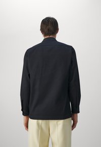 Black button-up shirt with long sleeves, a folded collar, and buttoned cuffs. Smooth fabric, straight cut, and minimal design.