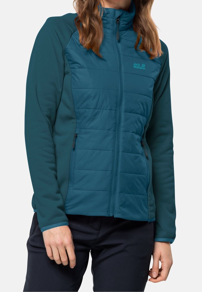 Veste isolante bleu sarcelle avec un devant matelassé, un design élégant et des manches en tissu doux équipées de poches zippées pour le rangement.