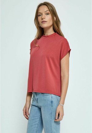 Top rosso corto con collo alto e maniche a cappuccio, realizzato in materiale morbido. Abbinato a jeans azzurri chiari, creando un look casual.
