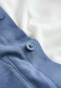 Tela de algodón azul con textura suave, que presenta un botón grande azul y un fondo de tela blanca. Detalles de costura sutiles visibles.