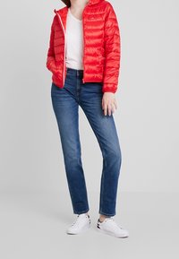 Czerwona pikowana kurtka puchowa z zamkiem błyskawicznym, zestawiona z niebieskimi prostymi jeansami i białymi trampkami. Pod spodem prosta biała koszulka.