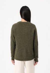 Maglione verde oliva con finitura testurizzata, scollatura rotonda e maniche lunghe. L'orlo è leggermente più lungo sul retro.