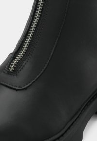 Bottine en cuir noir avec fermeture éclair argentée à l'avant et coutures visibles le long des bords.