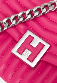 Vaaleanpunainen päällystetty nahkainen olkalaukku, jossa on hopeinen ketjuhihna ja suorakulmainen metallinen logolevy, jossa on selkeästi esillä "HUGO".