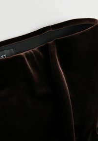 Gros plan sur la ceinture d'un pantalon en velours marron foncé avec un élastique noir à l'intérieur et une petite étiquette noire partiellement visible.