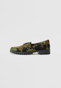 Loafers med camomønster laget av myk, teksturert stoff, med gulløyne og en robust svart gummisåle. Flat design.