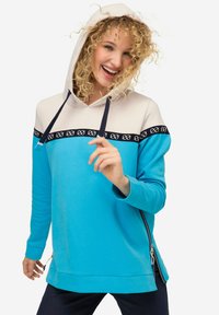 Sweat-shirt à capuche bleu clair avec un haut crème, une bande d'accent marine et une fermeture éclair sur le côté. Texture douce, design décontracté, adapté à diverses occasions.