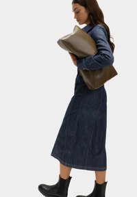 Jeansklänning, mörkblå, långärmad, knälång, rak skärning, bärs med svarta ankelskor, håller en brun läderclutch.