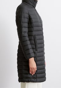 Sort vatteret frakke med høj krave, vandret quiltet mønster, to sidelommer og en knælængde skæring. Glat, skinnende tekstur.