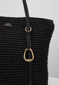 Sac cabas tissé noir avec une bandoulière en cuir noir et des ferrures dorées, comportant une petite étiquette portant l'inscription « Lauren Ralph Lauren ».
