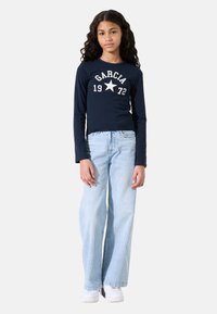 Marineblauwe longsleeve shirt met witte opdruk "GARICA 1972" en ster. Gecombineerd met lichtblauwe aansluitende jeans en witte sneakers.