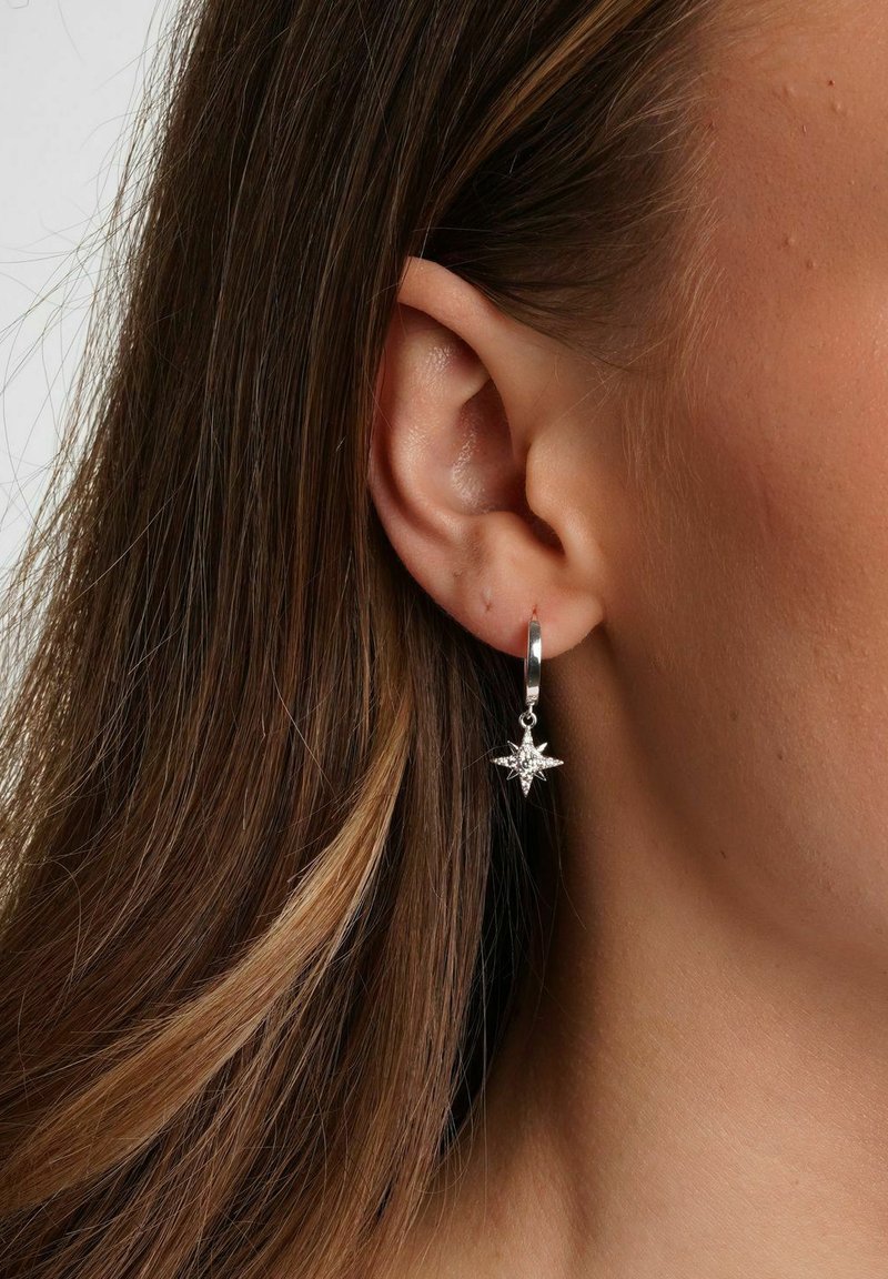 Silver hoopörhänge med en stjärnformad hänge som har en central ädelsten. Slät yta och polerad finish. Bärs på en modells öra.