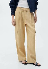 Lichtbeige wijde cargobroek met een drawstring taille, zijzakken en textured stof. Gecombineerd met zwarte sandalen.