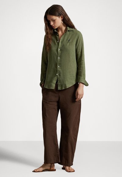 Zaļa lina krekls ar pogām un uzruļāmiem piedurknēm, kopā ar brūnām vaļīgām biksēm. Tajā ir neliels logo un gluda faktūra. Ikdienišķs piegriezums.