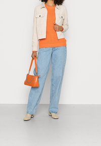 Lichtbeige corduroy jasje, feloranje gebreide trui, lichtblauwe wijde jeans en een oranje laktas met zilveren kettingdetail.