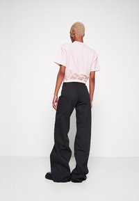 Camiseta corta de color rosa claro con cintura fruncida, combinada con pantalones anchos negros. Los pantalones tienen bolsillos traseros y una superficie texturizada.