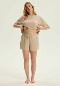Beżowy zestaw odzieży domowej składający się z luźnej koszulki z krótkim rękawem oraz szortów na elastycznej talii, wykonany z miękkiego materiału o gładkiej powierzchni.