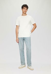 Witte katoenen T-shirt met een ronde hals, gecombineerd met lichtblauwe rechte spijkerbroeken en beige sneakers met witte accenten.
