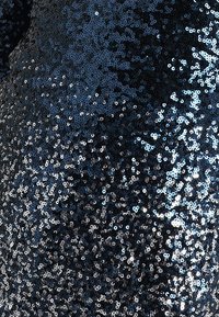 Mörkblått tyg täckt av tätt packade runda paljetter, som reflekterar ljus med en strukturerad glans. Mönstret är enhetligt med en glittrande effekt.