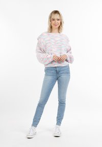 Maglione lavorato a maglia in tonalità pastello, con una vestibilità comoda e maniche ampie, abbinato a jeans azzurri e sneakers bianche.