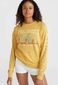 Felpa gialla con una grafica di quattro figure accanto a una tavola da surf, con la scritta "O'Neill Moments" e maniche lunghe bianche con testi decorativi.