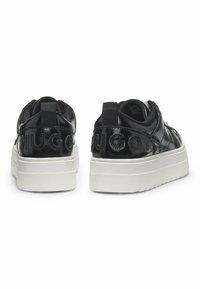 Black patent leather sneakers with a white platform sole and embossed "HUGO" logo on the back. Features textured panels and pull tab.