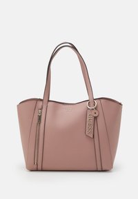 Sac à main mauve Guess avec deux anses, poche zipper verticale à l'avant et étiquette de marque suspendue à une anse sur fond blanc.