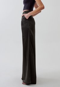 Pantaloni neri in satin a vita alta con una texture liscia, design a gamba larga e tasche laterali, abbinati a un top corto.