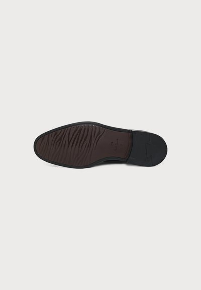 Semelle d’une chaussure formelle noire montrant une semelle extérieure texturée et à motif ainsi qu’une partie du talon avec les détails de la marque et de la taille.