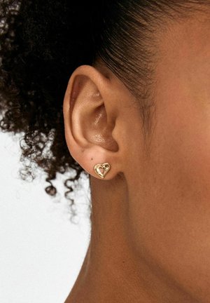 Goldene Ohrringe in Herzform mit offenem Design und glatter Oberfläche, getragen am Ohr einer Person, Nahaufnahme.