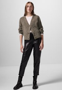 Suddig olivgrön cardigan med knäppning fram, worn över en ljus topp, ihop med glansiga svarta läderbyxor och kraftiga svarta kängor.