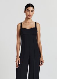 Tuta nera con un corpino aderente, scollatura quadrata e spalline spesse. Il tessuto ha una texture liscia, con dettagli di cucitura verticale lungo le gambe.