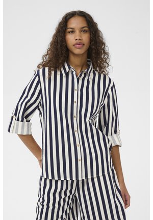 Navy plava i bijela prugasta košulja s dugmadima, s okovratnikom, podvrnutim rukavima i drvenim gumbima. Tkanina izgleda lagano i teksturirano.