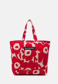 Sac en toile de coton rouge avec un grand motif floral, des accents crème, deux poignées et un patch logo noir. Forme rectangulaire avec un design carré.