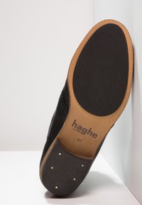 Suola nera di scarpa con una finitura liscia, caratterizzata da un bordo tan e piccoli chiodi dorati. Il logo impresso recita "haghe" e la taglia è "37".