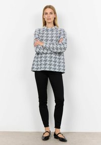 Szary sweter w wzór houndstooth o pudełkowym kroju, okrągłym dekolcie i długich rękawach, w połączeniu z czarnymi wąskimi dżinsami i płaskimi butami.