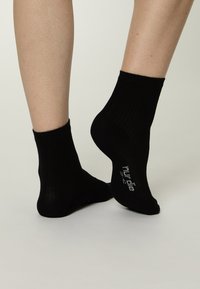 Schwarze Baumwollknöchelsocken mit geripptem Muster. Sie bieten eine enganliegende Passform und haben ein aufgedrucktes Größenetikett an der Sohle. Geeignet für den Alltag.