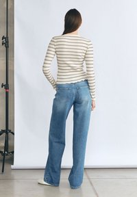 Lekka, prążkowana bluzka z długim rękawem w kolorze kremowym z granatowymi paskami, zestawiona z luźnymi jasnoniebieskimi dżinsami w klasycznym pięciokieszeniowym fasonie.