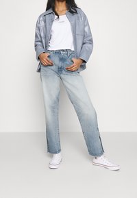 Chaqueta de imitación cuero azul claro sobre una camiseta blanca, combinada con unos vaqueros de cintura alta y desgastados de color azul y zapatillas blancas. Corte relajado y pierna recta.