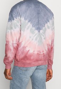 Felpa tie-dye con tonalità di grigio, rosa e verde, con colletto rotondo, maniche lunghe e polsini a coste. Morbida texture del tessuto.