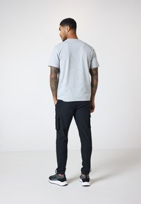 Camiseta gris de manga corta combinada con pantalones cargo negros que cuentan con bolsillos laterales y zapatillas grises con suelas blancas. Diseño sencillo y moderno.