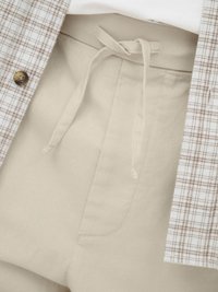 Pantalon beige avec un cordon en tissu noué à la taille, associé à une veste à carreaux marron clair et blanc avec un bouton visible.