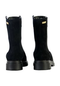 Bottines en daim noir avec une finition lisse, bout arrondi et semelle en caoutchouc plate ; présentent des accents en métal doré et des languettes de tirage.