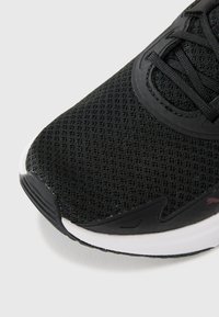 Black athletic shoe featuring a textured mesh upper, a smooth synthetic overlay, and a white midsole with a slight curve.