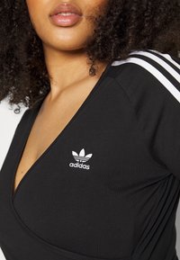 T-shirt de sport noir avec un design à col en V, orné du logo Adidas blanc et de trois bandes blanches sur les épaules, fabriqué à partir d'un tissu lisse.