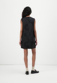 Black sleeveless dress with abstract dark pattern, straight cut, knee-length, and center back zipper. Worn with beige socks and black shoes.
