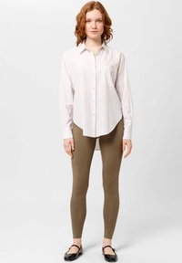 Overhemd met lichtroze en witte strepen, gecombineerd met aansluitende olijfgroene leggings en zwarte ballerina's. Minimalistisch ontwerp.