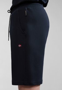 Bermudas deportivas de color azul marino en tejido suave, con una cinturilla elástica, bolsillos laterales y un pequeño logo bordado de la bandera en la pierna izquierda.