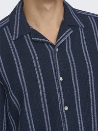 Chemise bleu marine à boutons avec des rayures blanches verticales, tissu texturé, col à revers et deux boutons au plastron.
